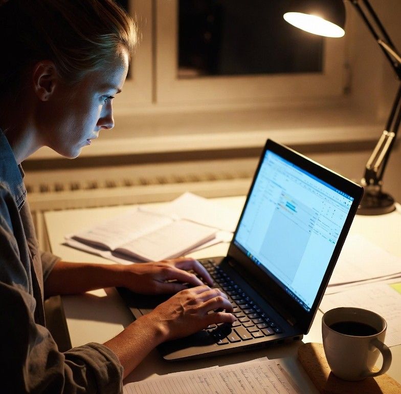 young professional working on a laptop at night with budgeting notes and coffee beside them
